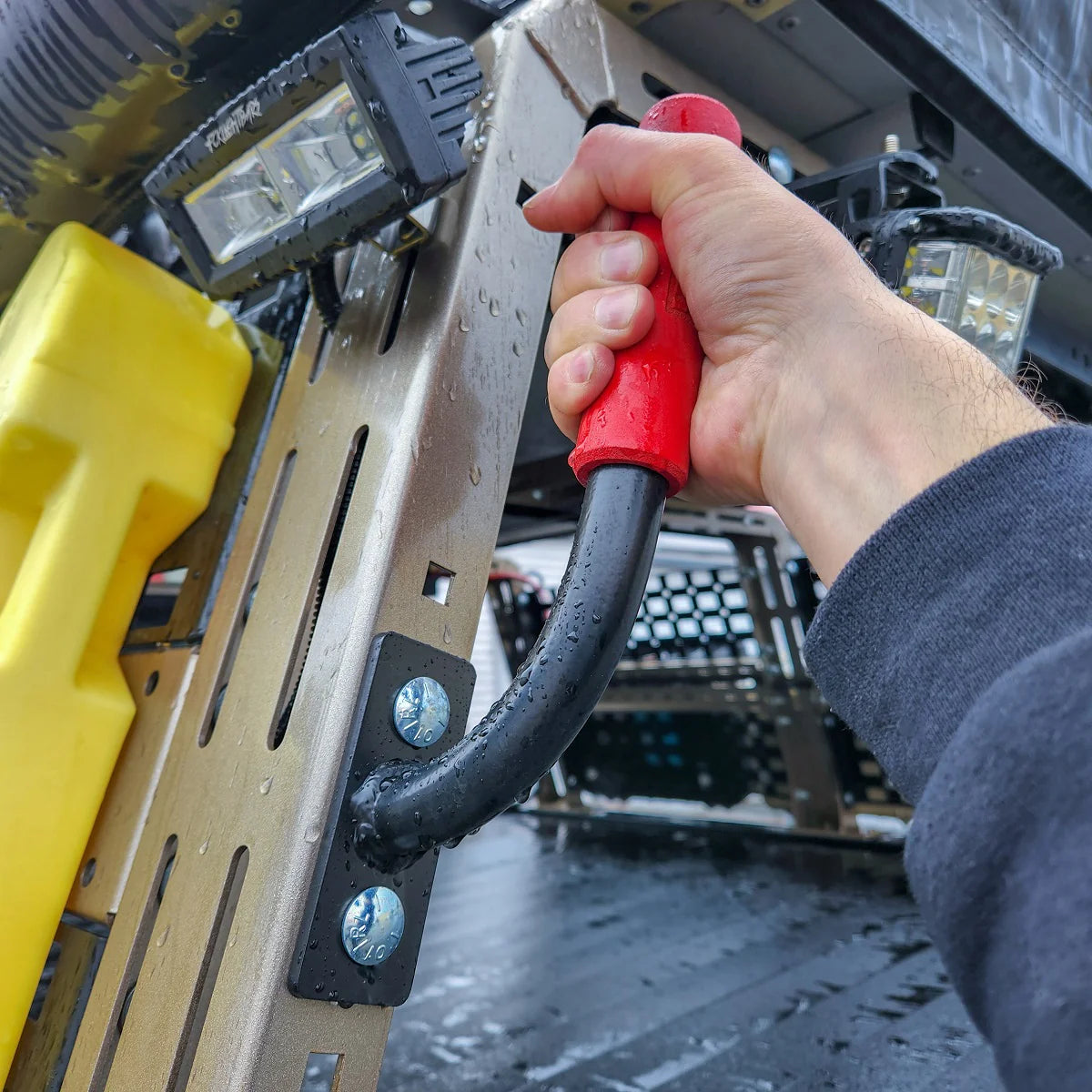 Hand gripping a red Heavy Metal Off-Road grab bar on a vehicle rack