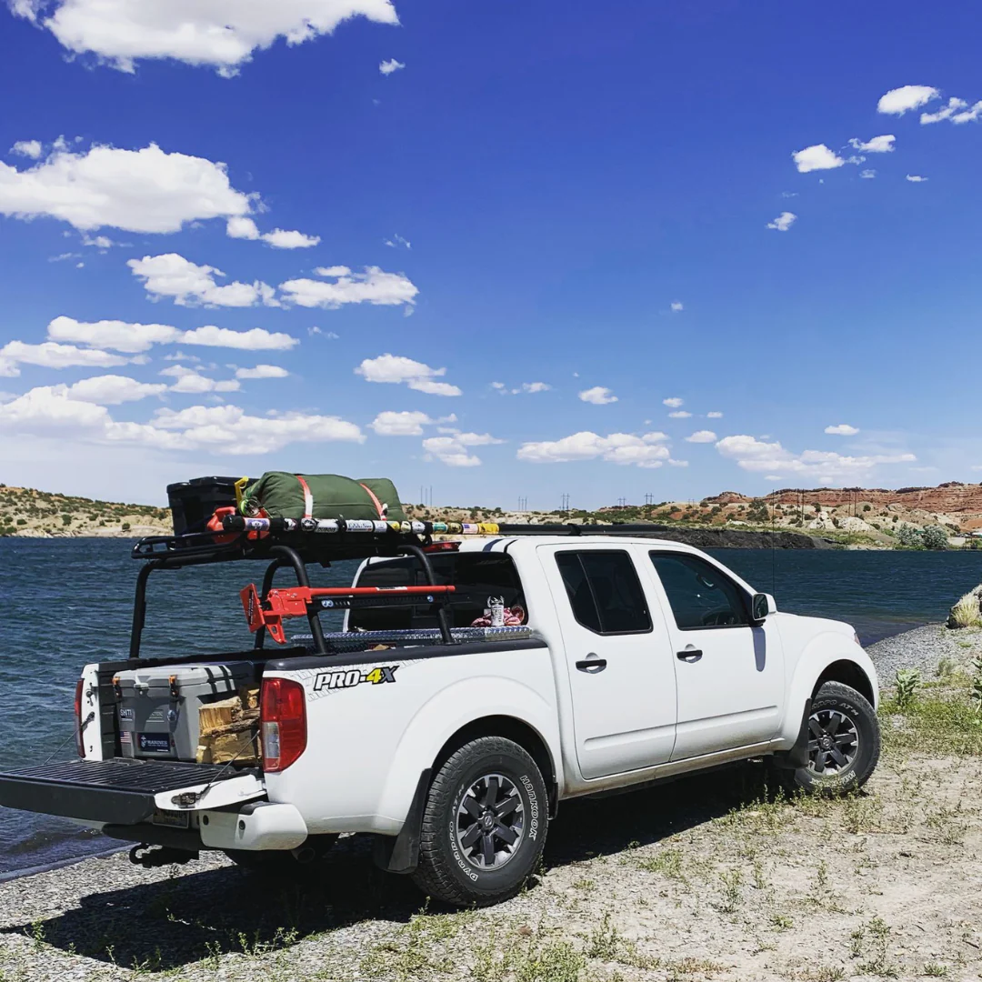White pickup with an overland bed rack beside a lake