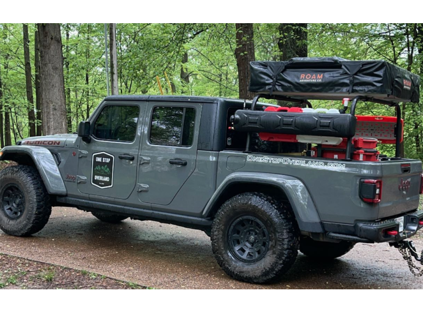 Gray Jeep Gladiator with an overland rack and camping gear in the woods