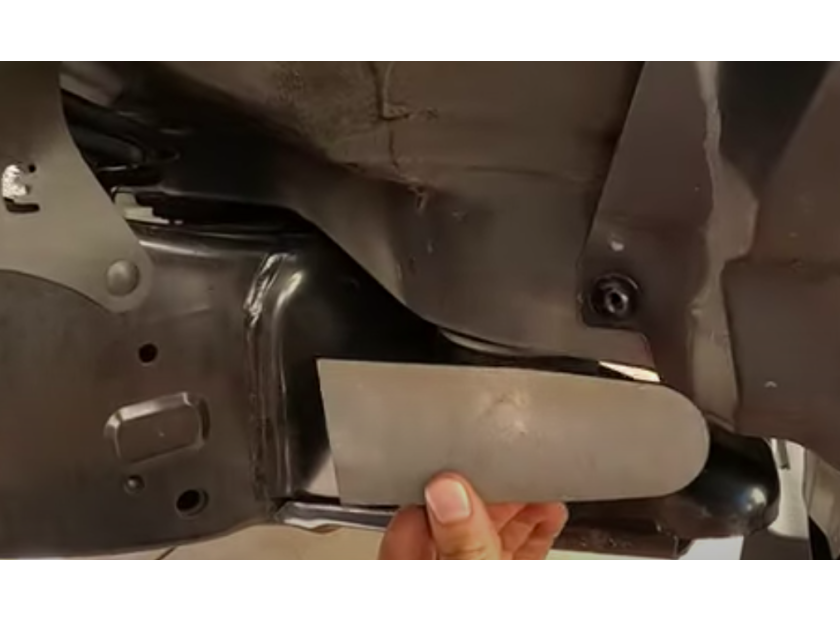 Hand positioning a metal cab mount chop plate against a Toyota truck frame