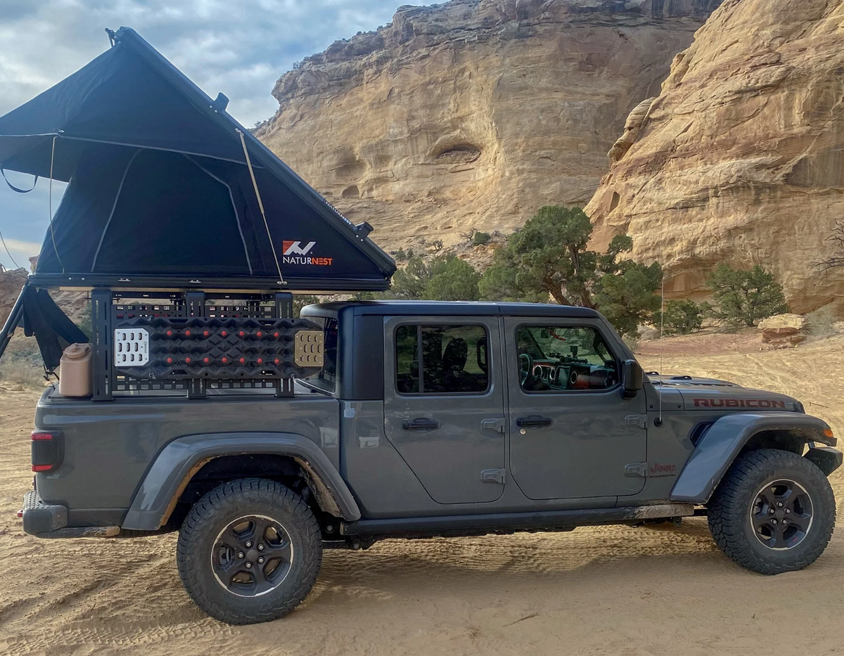 Gray Jeep Gladiator with rooftop tent beside desert rock formations