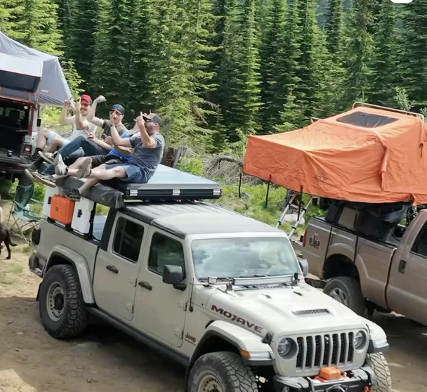 People standing on two Jeeps equipped with rooftop tents at an expo