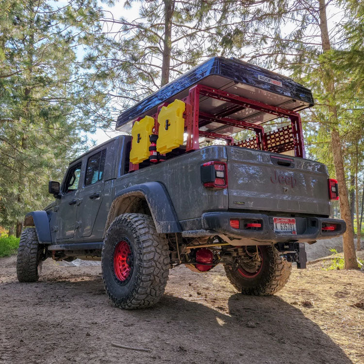 Gray lifted Jeep Gladiator with an overland bed rack in the woods