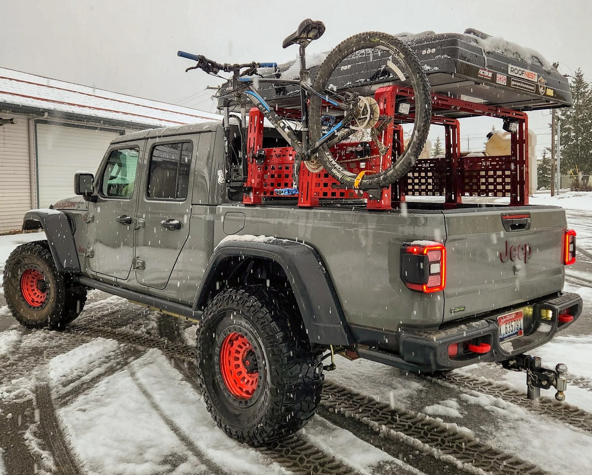Gray Jeep Gladiator with a bicycle mounted vertically on its bed rack in the snow
