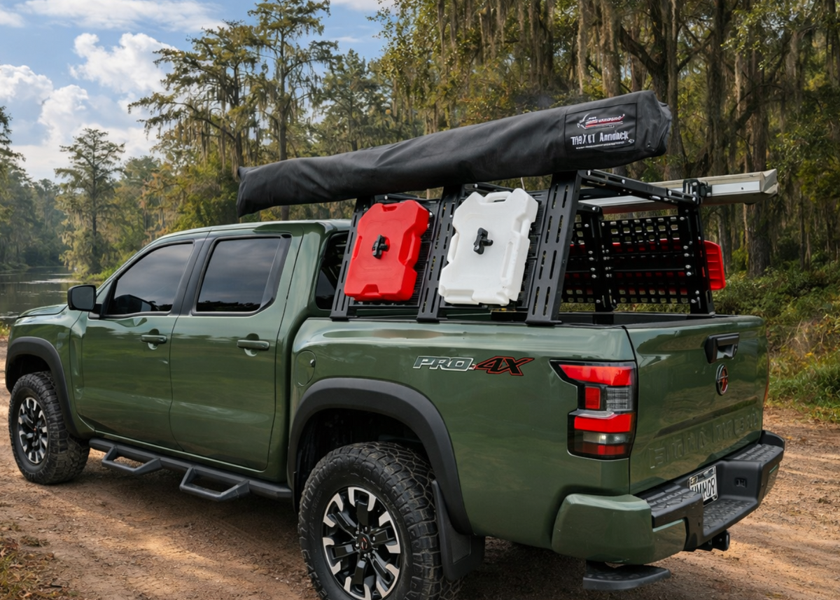 Green Nissan Frontier with a Heavy Metal Off-Road bed rack, rooftop tent, and mounted fuel cans in the woods
